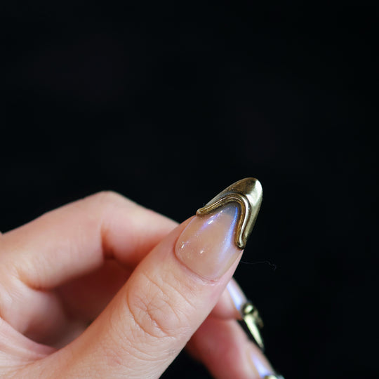 Golden Drip press-on nails on hand, soft nude base with gold French tips and sculpted raised lines, glossy close-up.