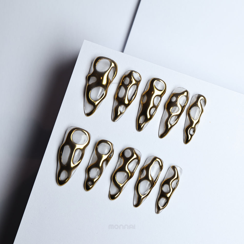 Golden Flow press-on nails with liquid-metal gold openwork on milky white, shown laid out in close-up.