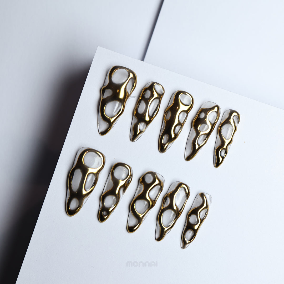 Golden Flow press-on nails with liquid-metal gold openwork on milky white, shown laid out in close-up.
