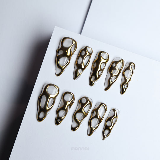 Golden Flow press-on nails with liquid-metal gold openwork on milky white, shown laid out in close-up.