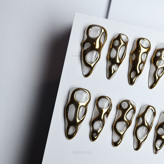 Golden Flow press-on nails with liquid-metal gold openwork design and glossy reflective finish, laid out on white.