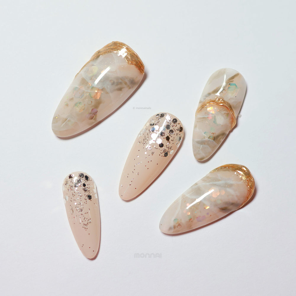 Golden Marble press-on nails laid out, creamy beige marble with iridescent flakes, glitter, and metallic gold accents