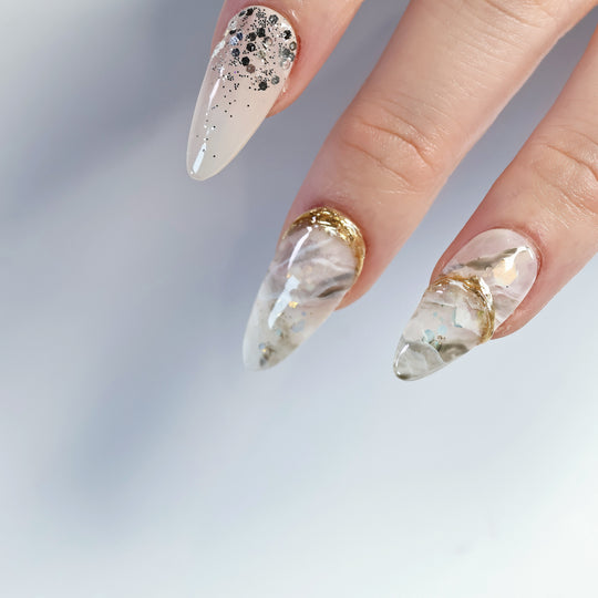 Golden Marble press-on nails on hand with creamy beige smoky stone design, gold accents and glitter
