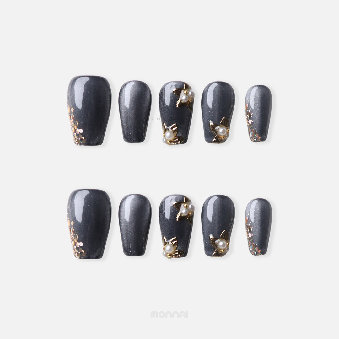 Golden Pearl Noir press-on nails with charcoal shimmer, gold glitter tips, and pearl floral accents