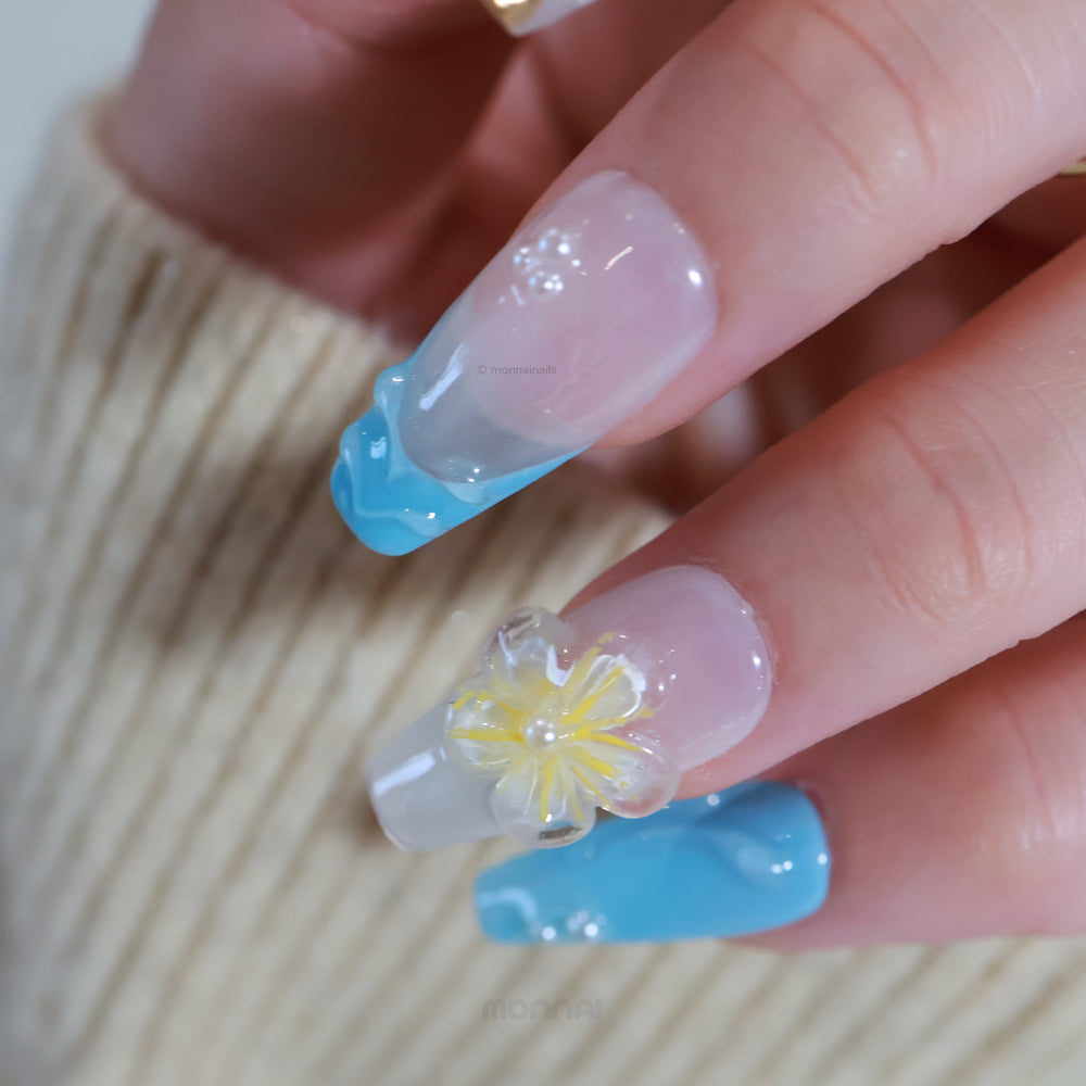 Golden Shore press-on nails on hand with milky white base, teal wavy French tips, and translucent floral accent.
