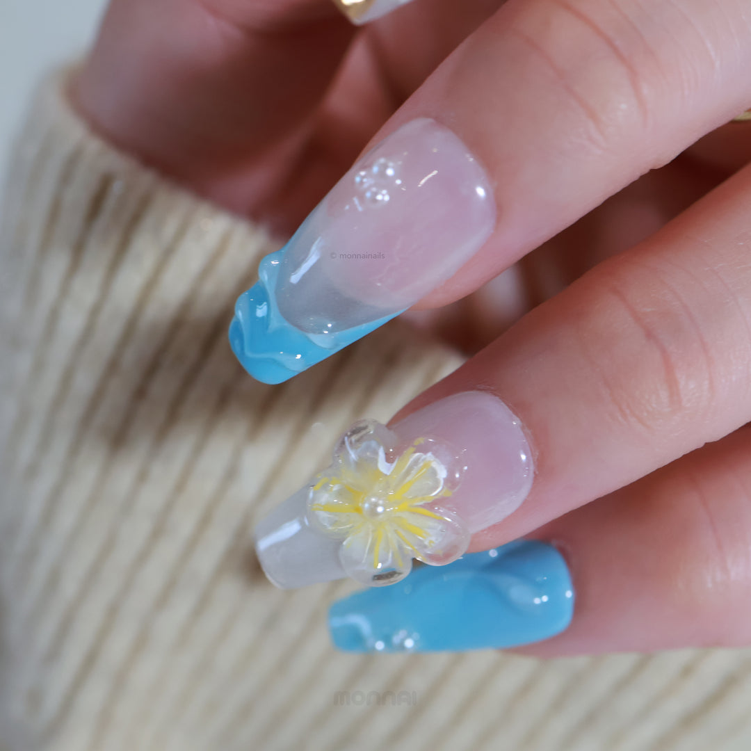 Golden Shore press-on nails on hand with milky white base, teal wavy French tips, and translucent floral accent.