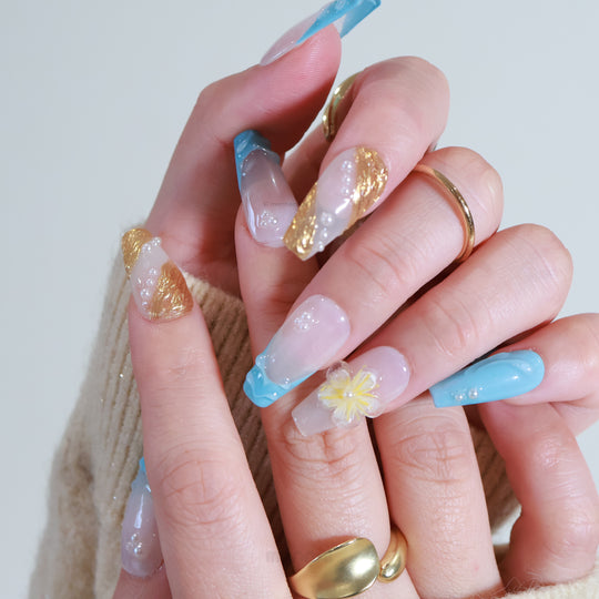 Golden Shore press-on nails worn on hands, with milky white bases, teal French tips, gold accents and a translucent floral motif.