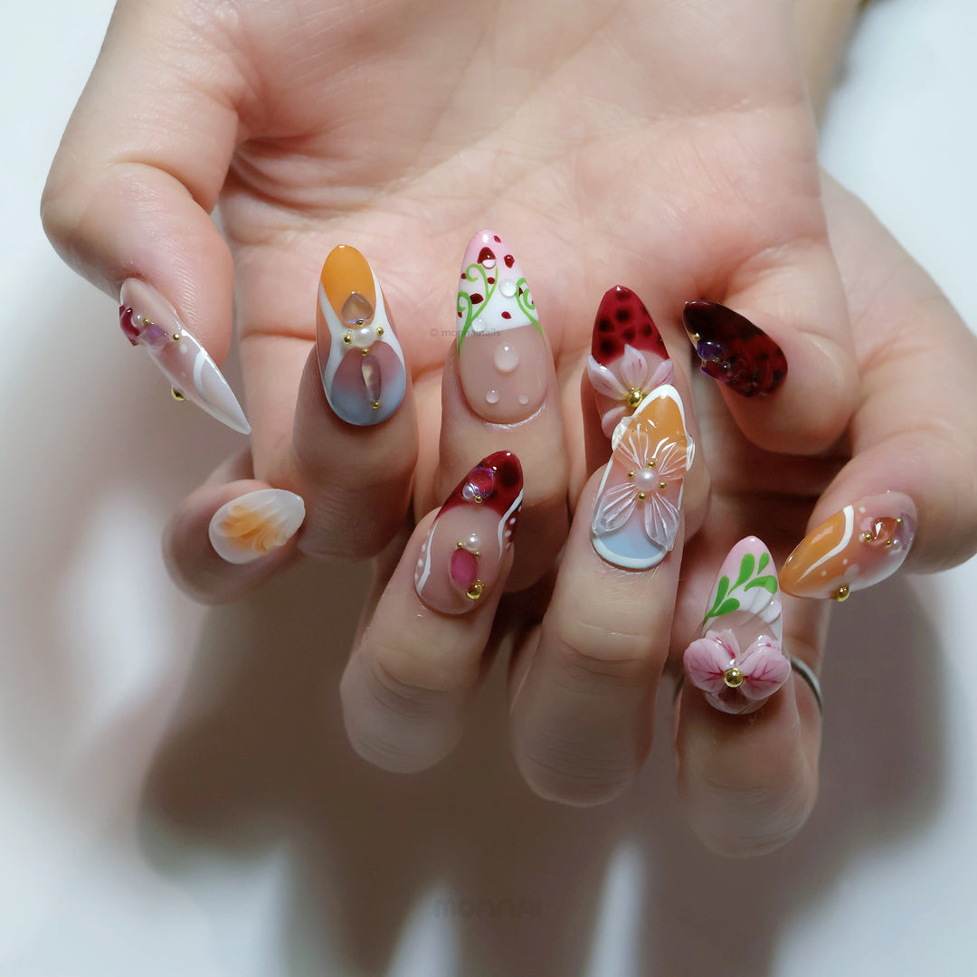 Grace press-on nails worn on hands, showing vintage florals with nude bases, red accents, and gem details.