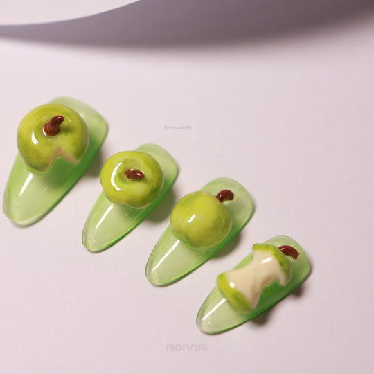 Green Apple press-on nails laid out in close-up, glossy green apple sculpted 3D details on soft green nails.