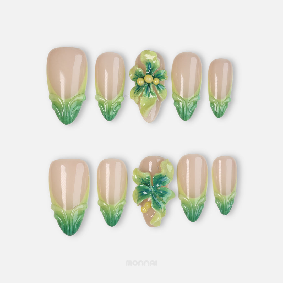 Green Bloom press-on nails laid out in close-up, sheer nude with soft green French tips and glossy 3D floral accents.
