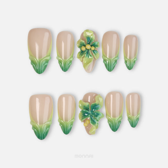 Green Bloom press-on nails laid out in close-up, sheer nude with soft green French tips and glossy 3D floral accents.