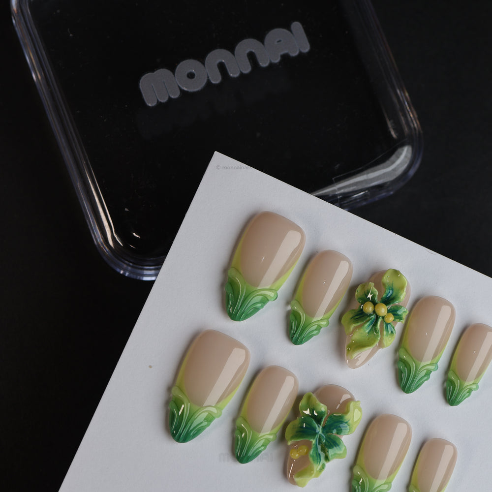 Green Bloom press-on nails laid out with sheer nude bases, soft green French tips, and 3D floral accents