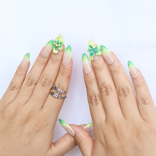 Green Bloom press-on nails worn on hands, sheer nude with green French tips and 3D floral accents.