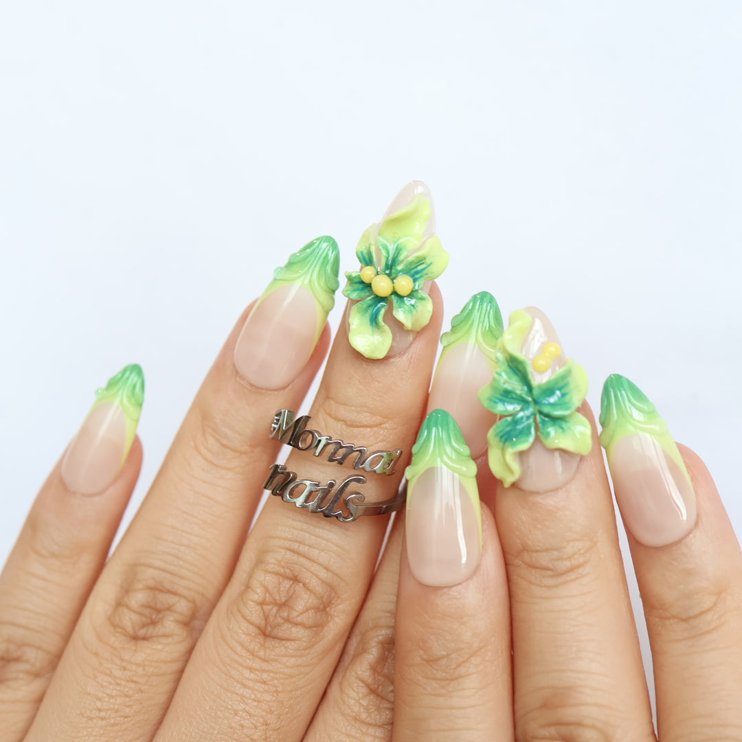 Green Bloom press-on nails on hands, sheer nude bases with green French tips and 3D floral accents in fresh floral detail.