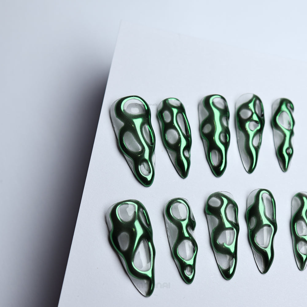 Green Flow press-on nails laid out, featuring sculptural metallic green chrome on a clear base.