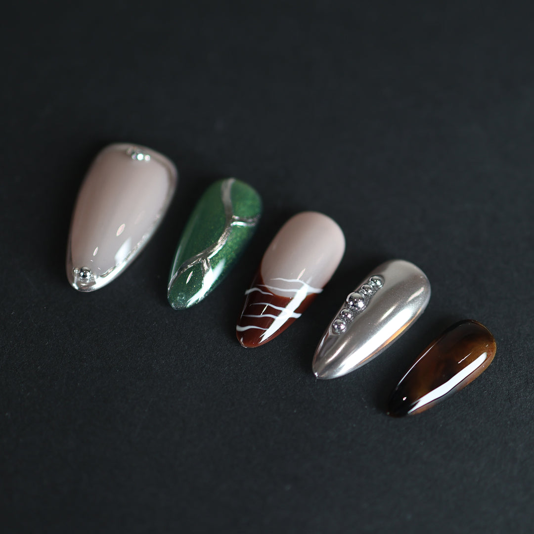 Green Light press-on nails laid out with forest green cat-eye, silver chrome, amber tortoiseshell, and marble veining