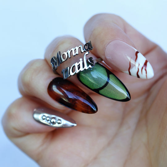 Green Light press-on nails worn on hand, with forest green cat-eye, amber tortoiseshell, chrome accents, and marble veining.
