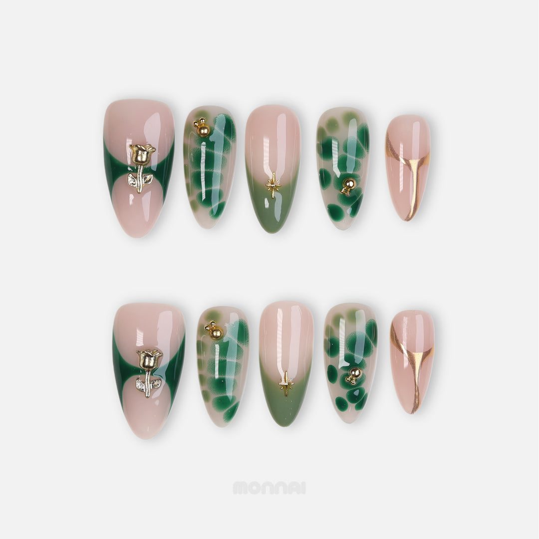 Green Swan press-on nails laid out in two rows, with sheer nude, emerald abstract details, gold lines, and sculpted gold rose accents.