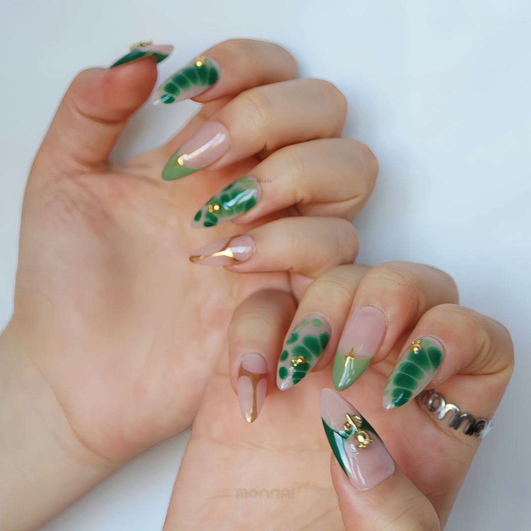 Green Swan press-on nails worn on hands, with sheer nude base, emerald green abstract details and gold accents.