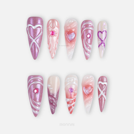 Heart’s Luster press-on nails shown laid out, with pink glitter hearts, glossy swirl details, and soft nude shimmer accents.