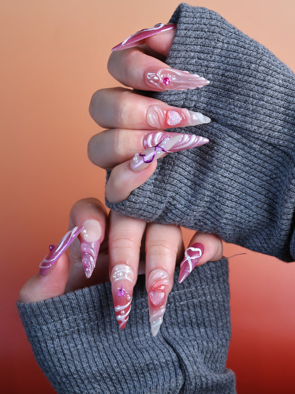 Heart’s Luster press-on nails worn on hands, with pink glitter, soft shimmer, glossy swirls, and heart motifs.