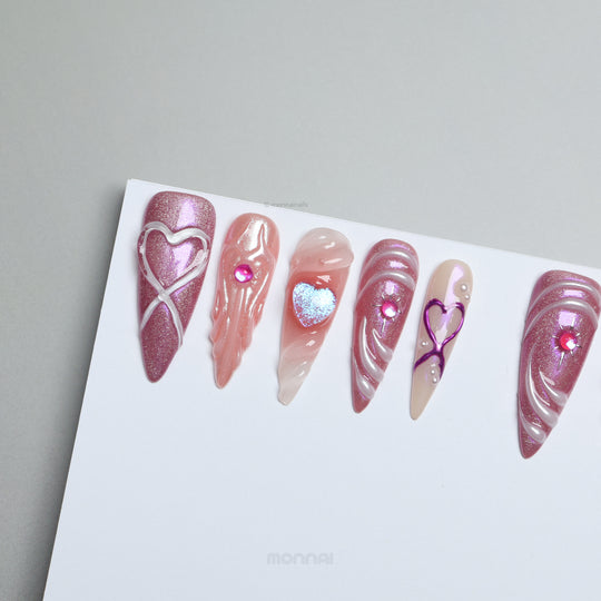 Heart’s Luster press-on nails laid out, with pink glitter, glossy heart motifs, sculpted swirls, and nude accents.