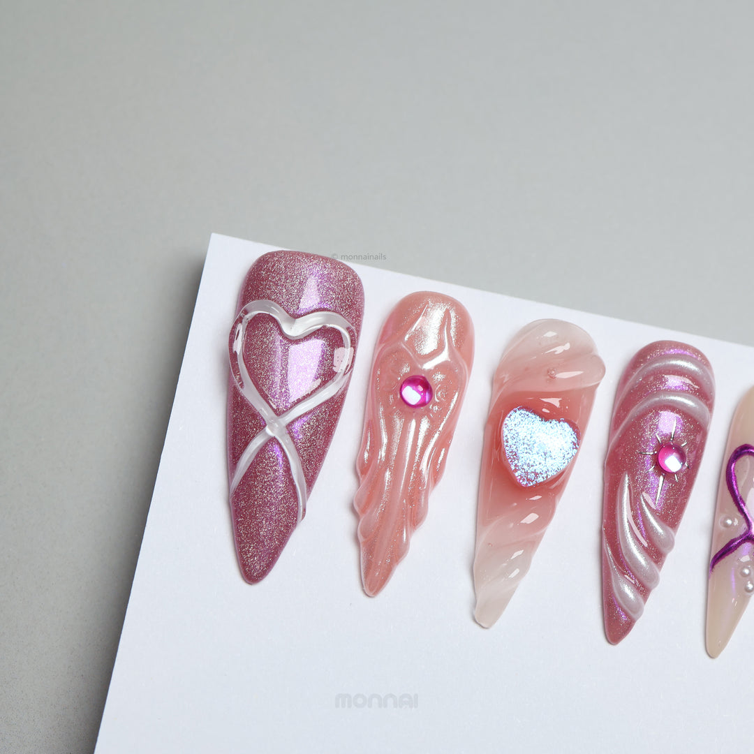 Heart’s Luster press-on nails shown laid out, with pink glitter, glossy swirl heart details, and soft nude tones.