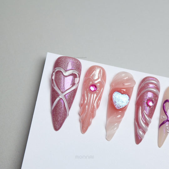 Heart’s Luster press-on nails shown laid out, with pink glitter, glossy swirl heart details, and soft nude tones.