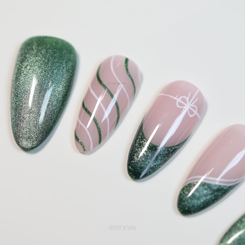 Holiday Cheer press-on nails with emerald cat-eye finish and soft pink ribbon line art, laid out in close-up