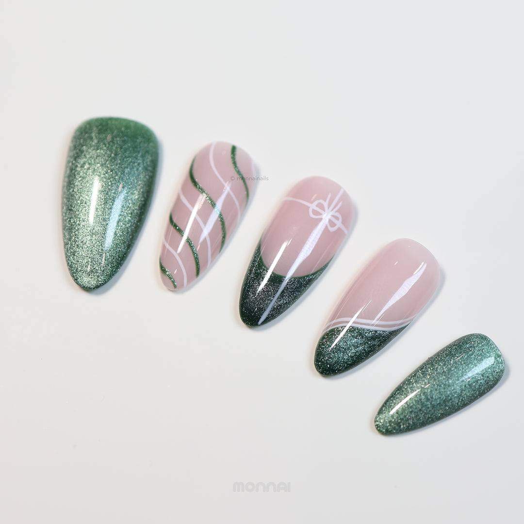 Holiday Cheer press-on nails laid out with emerald green cat-eye and soft pink ribbon line art.