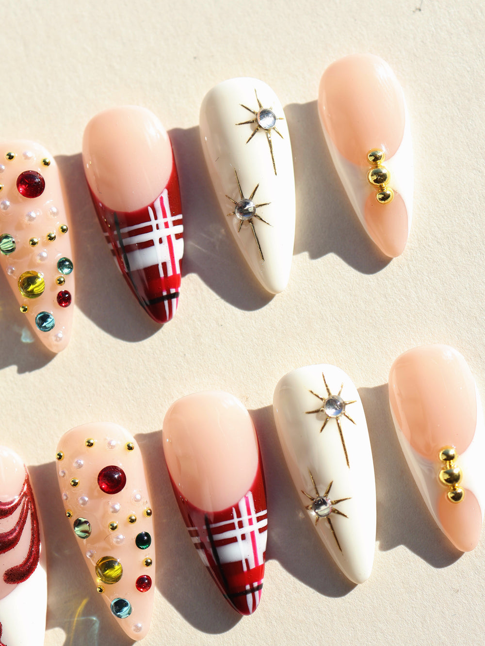 Holiday Glam press-on nails shown as a full set with nude, white, red tartan, gold starbursts, and gemstones.