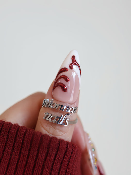 Holiday Glam press-on nails on hand, nude almond nail with red metallic swirls and glossy finish