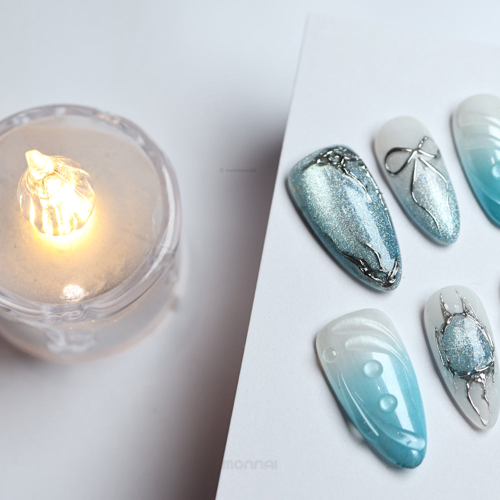Icy Bubble press-on nails in blue ombré and silver cat-eye shimmer with chrome details, laid out in close-up.