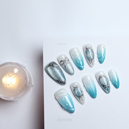 Icy Bubble press-on nails laid out, blue ombré with silver cat-eye shimmer and chrome details