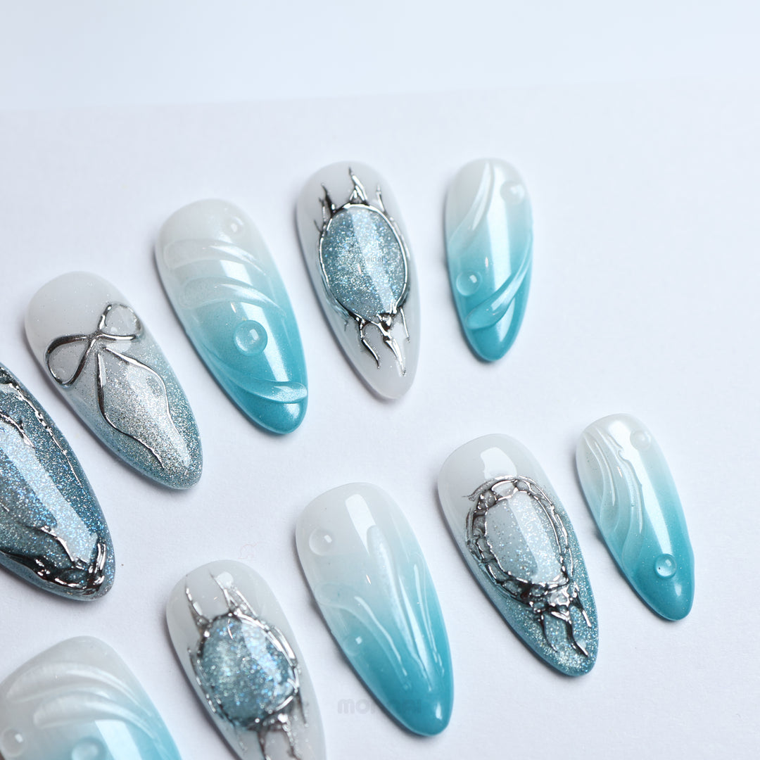 Icy Bubble press-on nails laid out in close-up, with blue ombré, silver cat-eye shimmer, and chrome details.