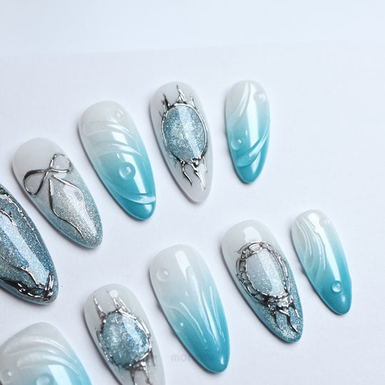Icy Bubble press-on nails laid out in close-up, with blue ombré, silver cat-eye shimmer, and chrome details.
