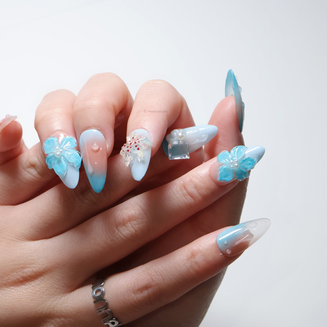 Icy Petals press-on nails worn on hand, with ethereal blue-and-blush 3D flowers and glossy gel accents