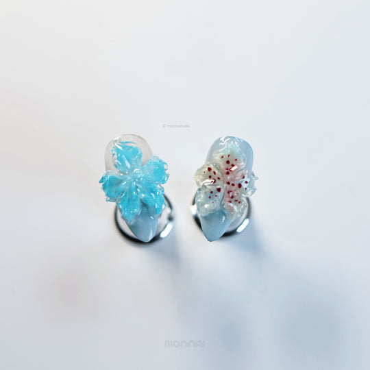 Icy Petals press-on nails laid out in close-up, with translucent 3D flowers and glossy blue blush accents.