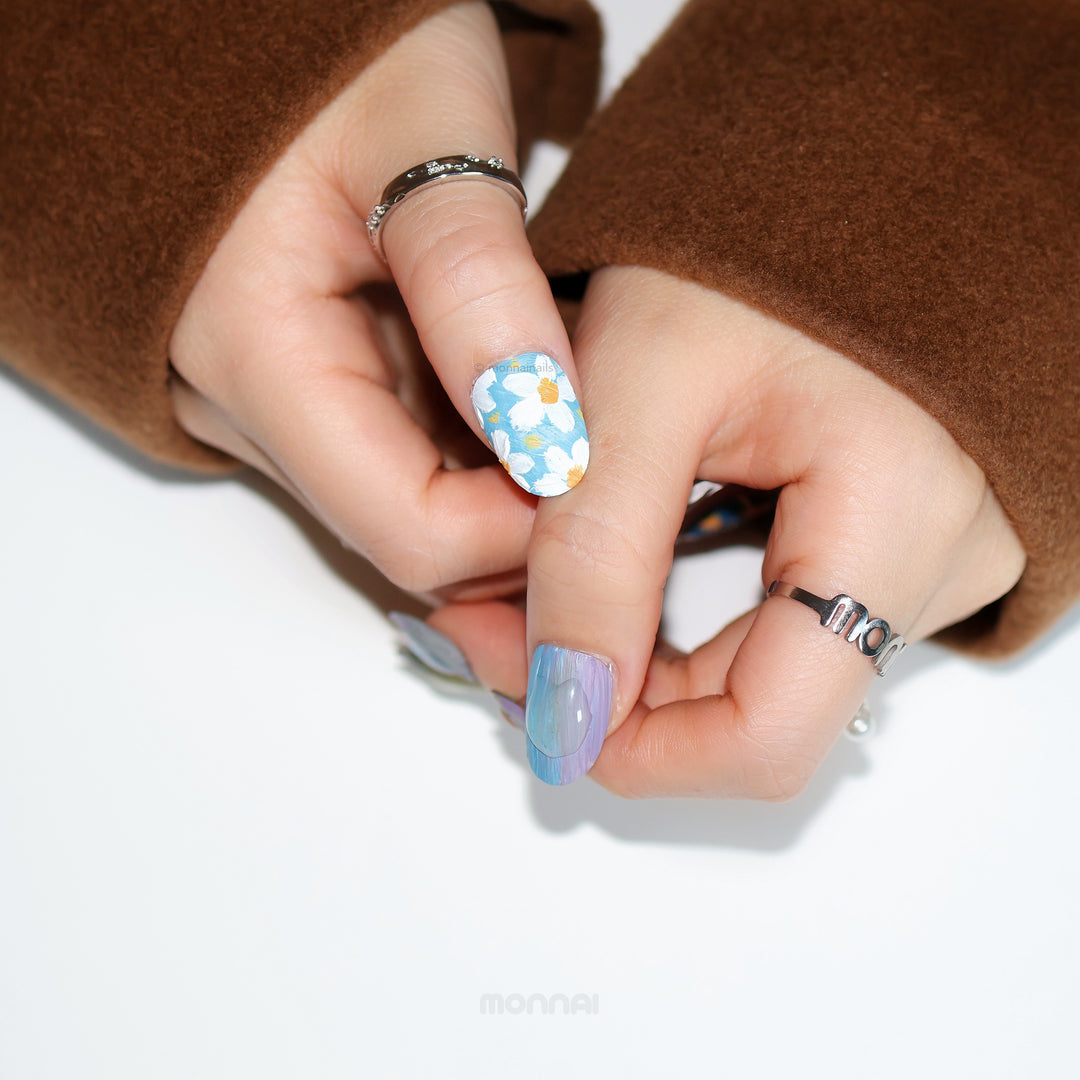 Impressionist Garden press-on nails worn on hand, featuring blue floral brushstrokes and a matte canvas-like finish.