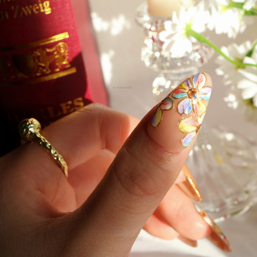 Iridescent Petals press-on nails on hand, close-up of pastel floral design with raised gold linework and glitter French tips