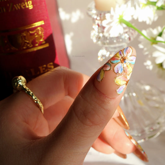Iridescent Petals press-on nails on hand, close-up of pastel floral design with raised gold linework and glitter French tips