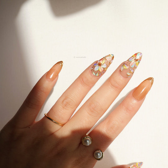 Iridescent Petals press-on nails worn on hand, with stained-glass floral petals and sheer peach glitter French tips
