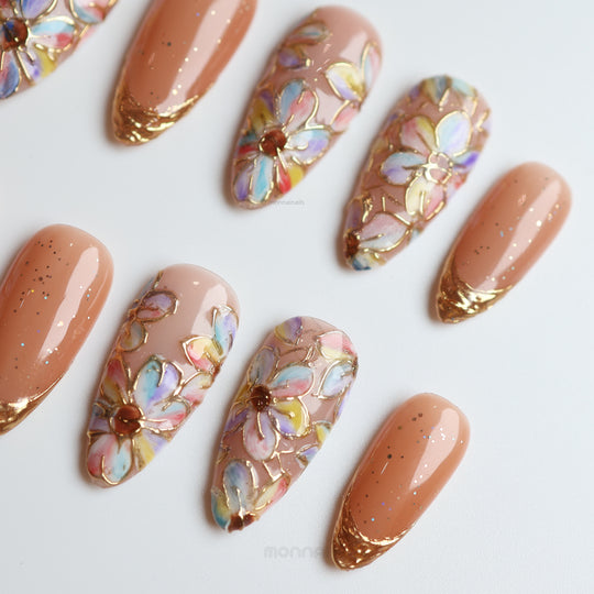 Iridescent Petals press-on nails with pastel watercolor florals, gold linework, and sparkling peach French tips laid out close-up