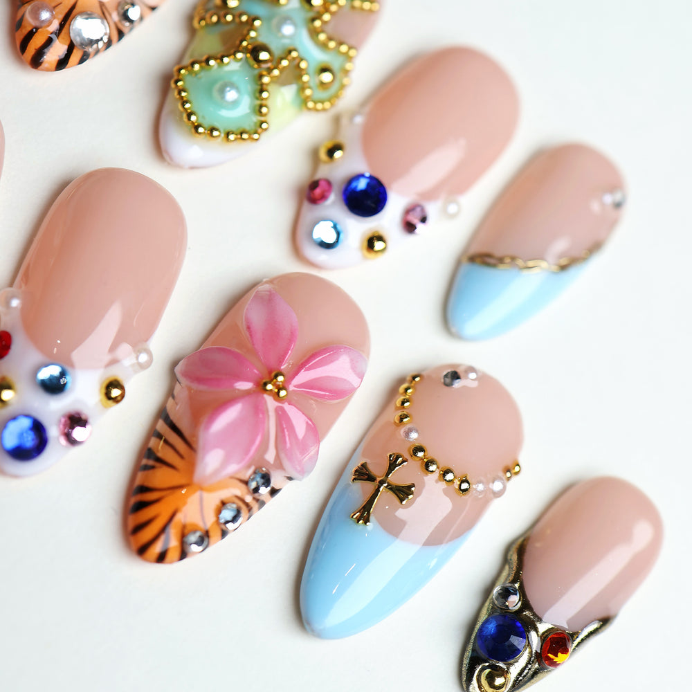 LUX press-on nails laid out in close-up with sky-blue tips, floral art, gold studs and colorful rhinestones