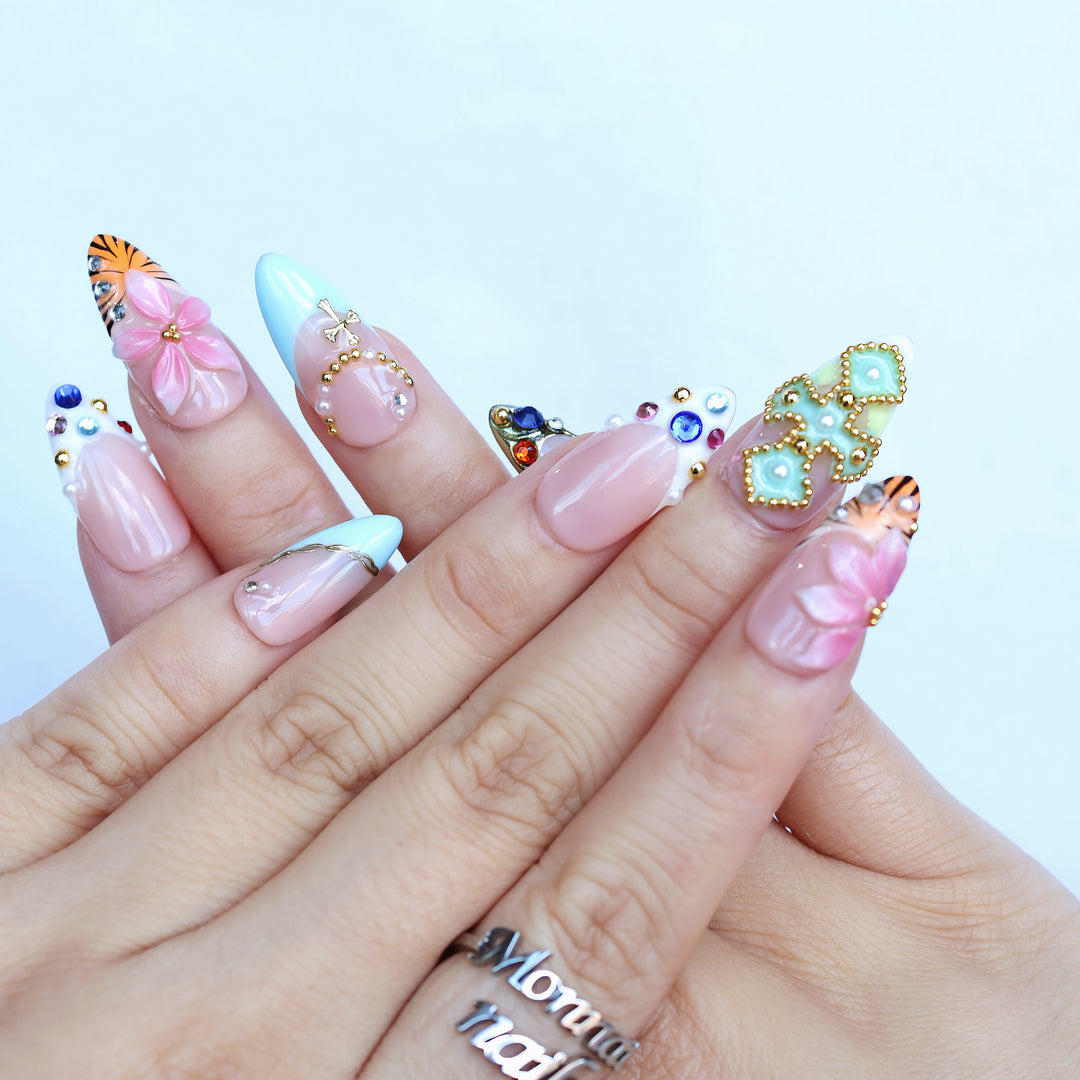 LUX press-on nails shown on hands with sky-blue French tips, floral art, rhinestones, and gold studs