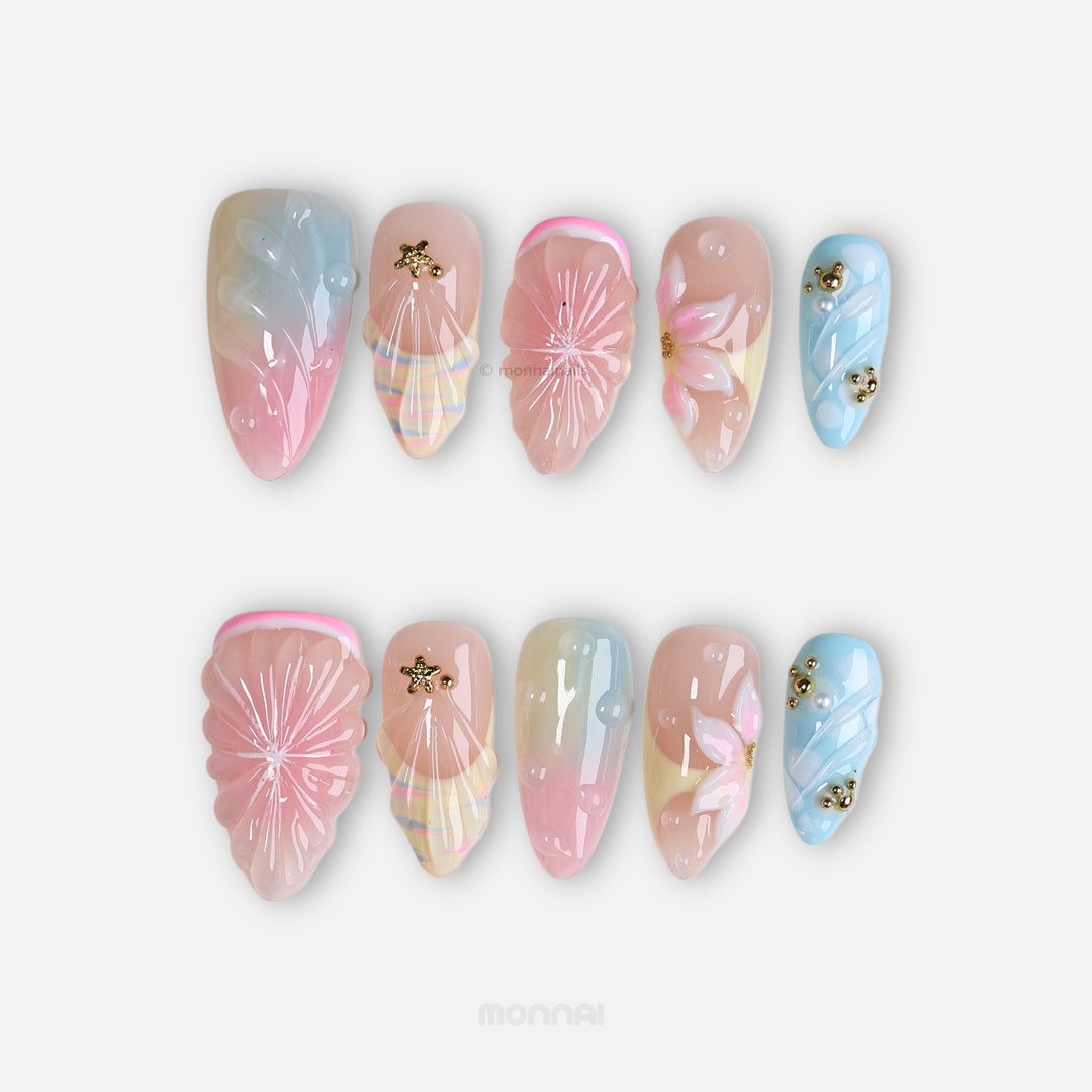 La La Land press-on nails laid out, pastel blush pink and sky blue with shell textures, floral accents, and gold charms.