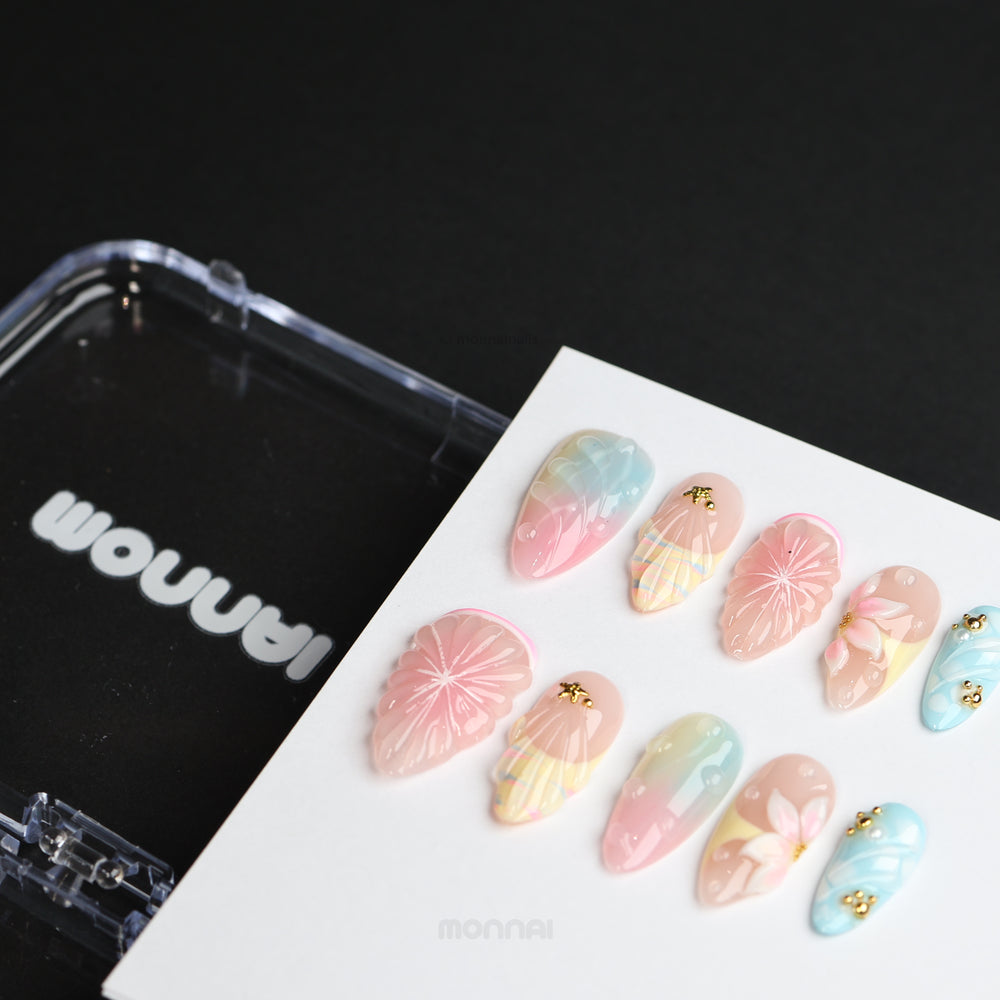 La La Land press-on nails laid out, showing pastel blush pink, sky blue and nude floral shell designs with gold charms.