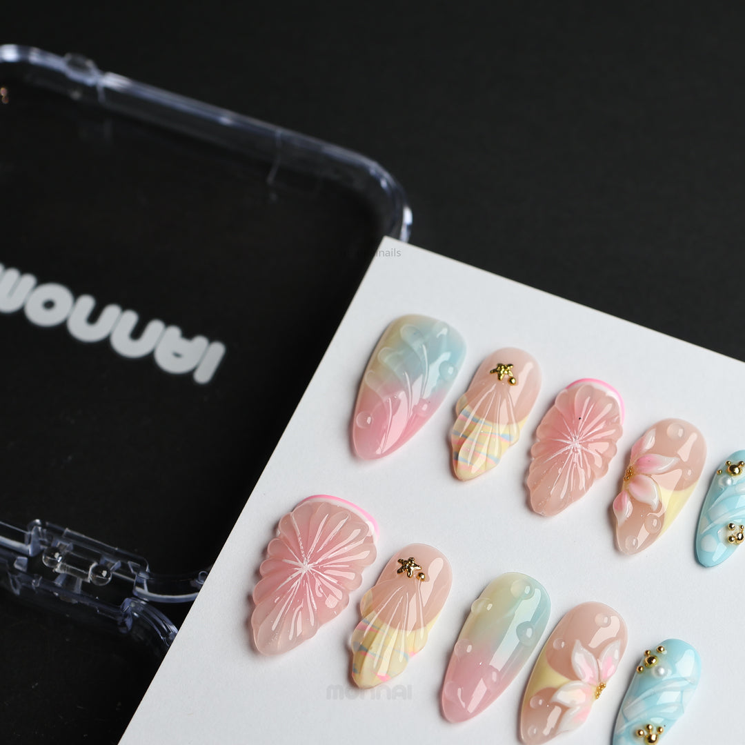 La La Land press-on nails laid out in pastel blush, blue and nude with floral accents, shell textures and gold charms