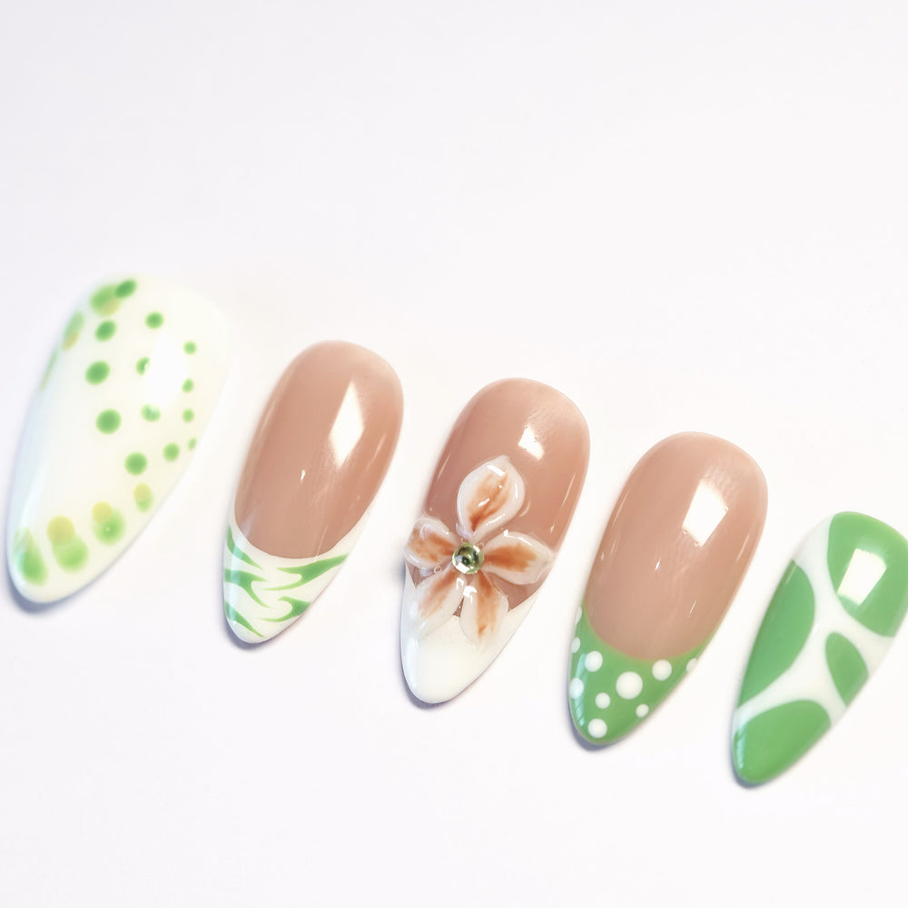 Leaf Dance press-on nails laid out with sage green polka dots, wavy French tips, and a 3D flower on a nude base