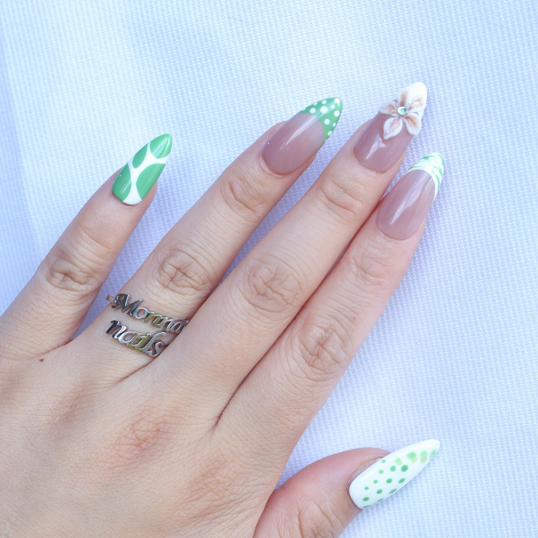 Leaf Dance press-on nails worn on hand, with muted sage green polka dots, wavy French tips, and a 3D flower on a nude base.